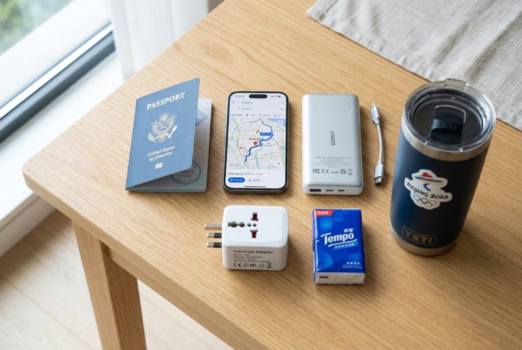 Neat flat-lay travel packing essentials for China including passport, smartphone with maps, power bank, plug adapter and tissues