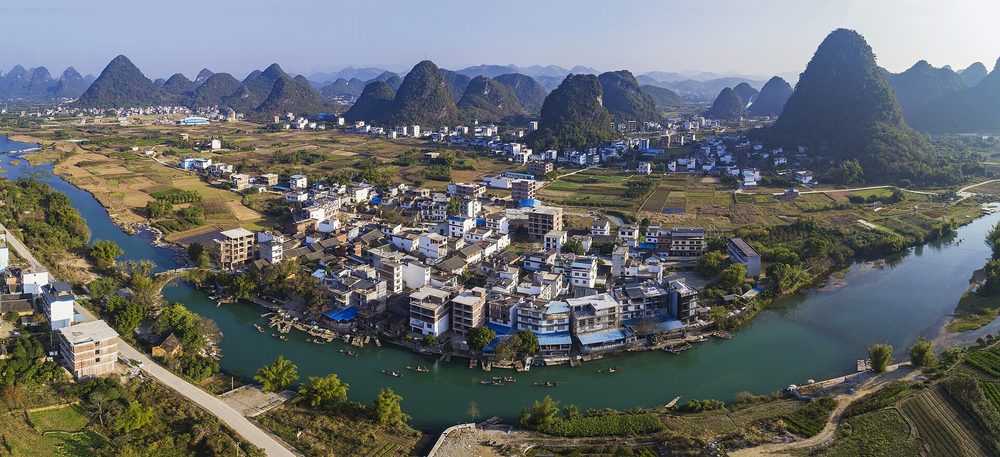 Reisende auf einem leisen Elektroroller entlang malerischer Reisfelder und Karstberge am Yulong-Fluss
