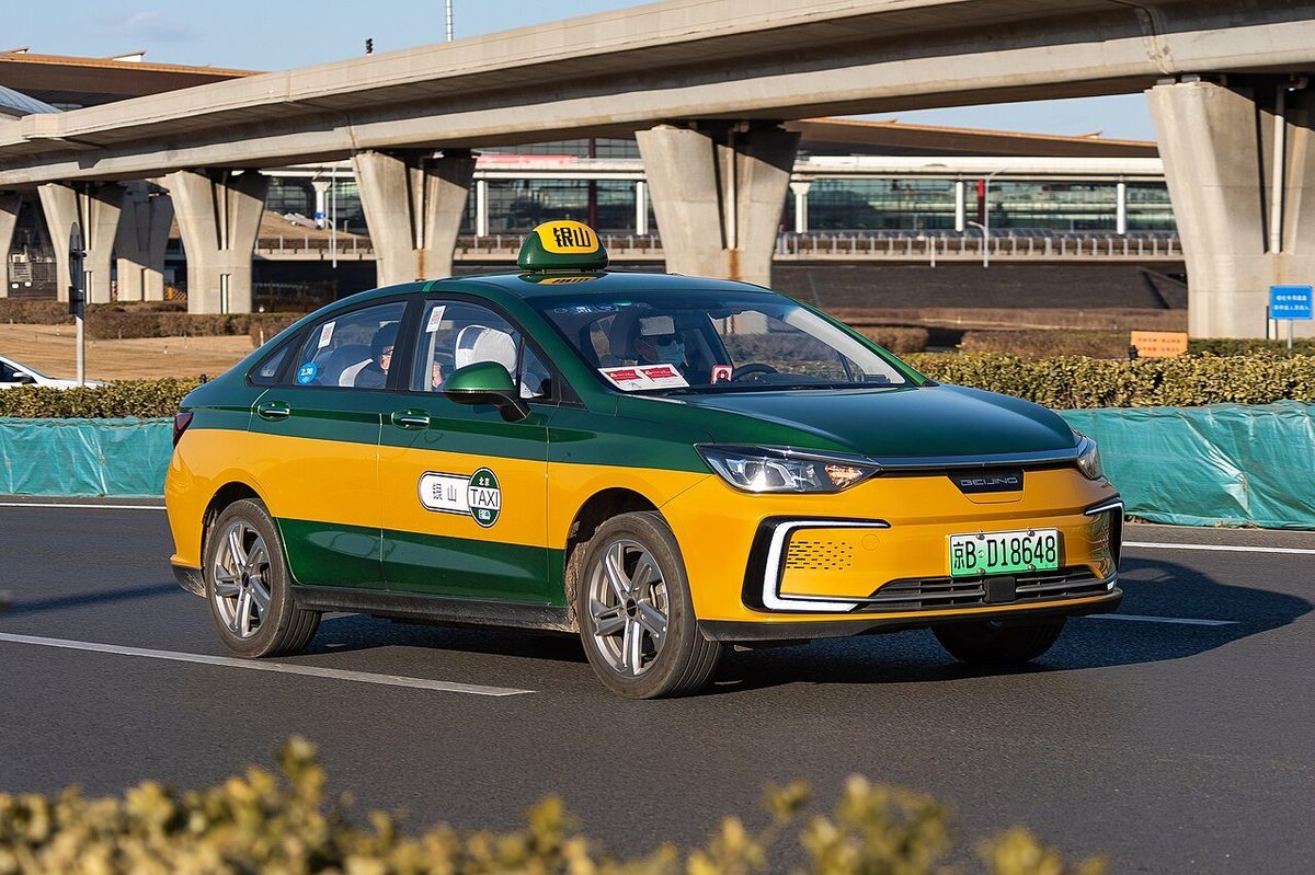 Official Beijing municipal electric taxi with yellow and dark livery driving out of Beijing Capital International Airport Terminal 3