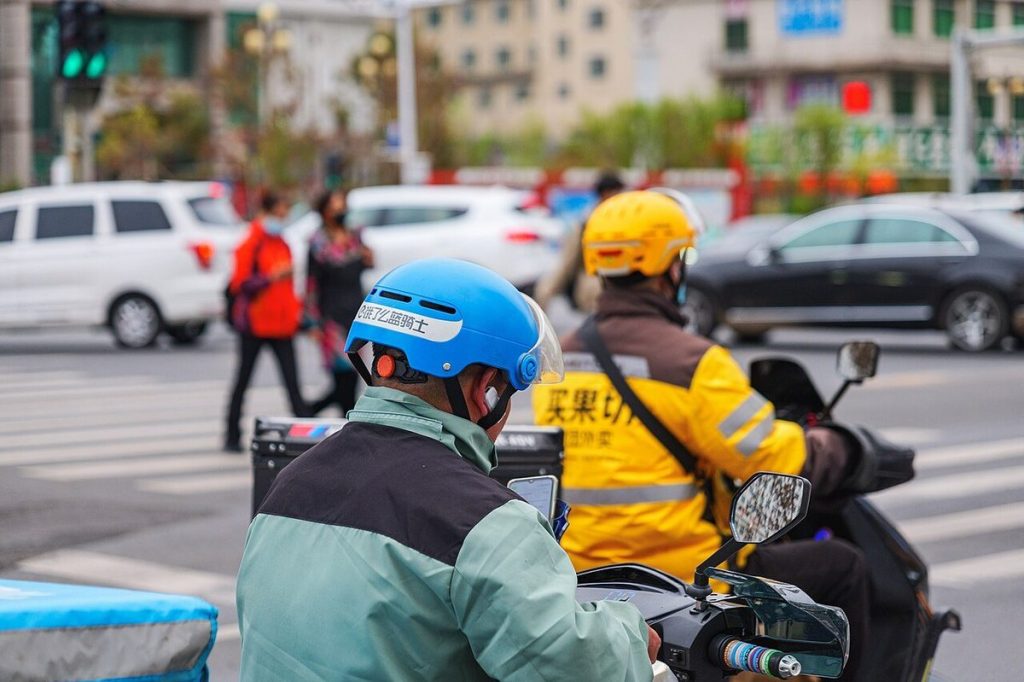 Meituan yellow-clad courier and Ele.me blue courier waiting on electric scooters with insulated food delivery boxes in China